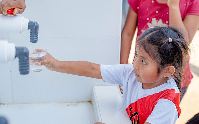 A young girl is pouring water into a clear glass.