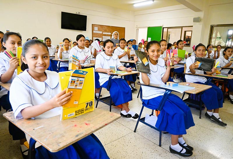 A group of school children, sitting at desks in a classroom setting with supplies provided by child sponsorship.