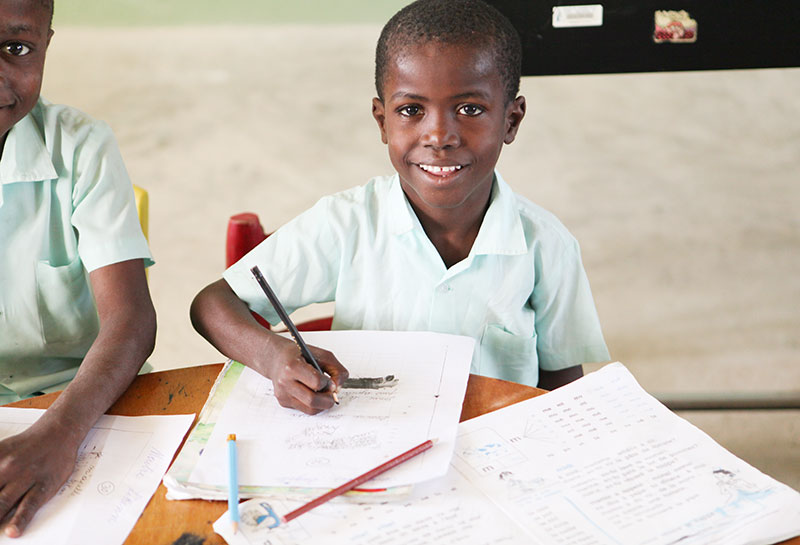 Two boys sitting at a table with papers and pencils provided by child sponsorship