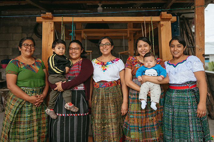 A group of women dressed in traditional attire smiles together for a photograph, showcasing their cultural heritage.