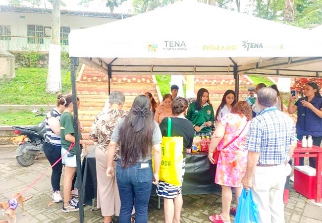 A group of people gathered around a table filled with various food created by young entrepreneurs in Colombia, under a white tent.